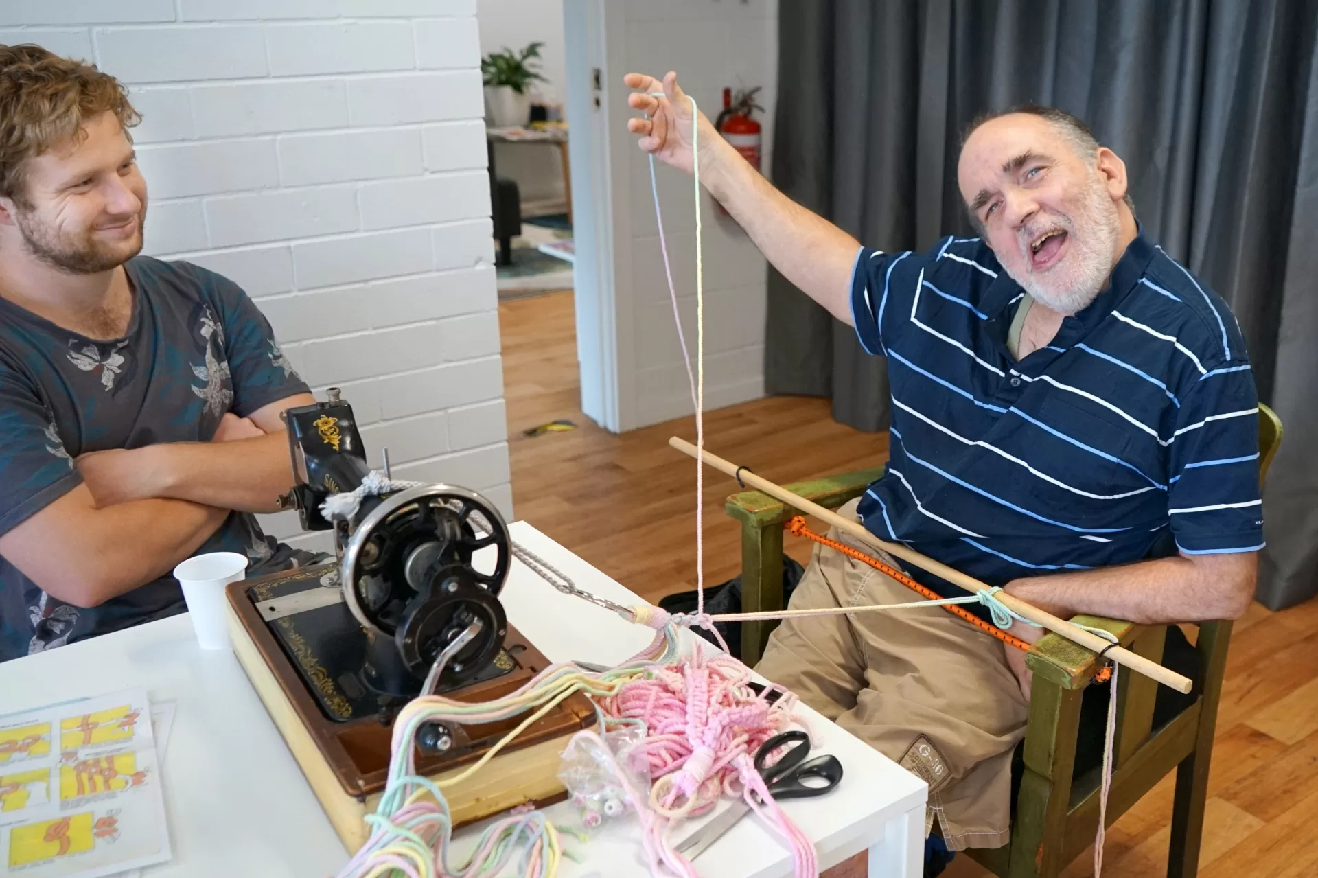 A man in a wheelchair smiles as he using macrame tools to craft