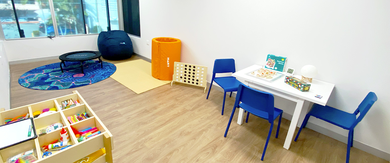 Allied Health therapy room with a blue rug, trampoline, bean bag, therapy tube, connect four, activity table with three seats and a drawer with arts & crafts materials.