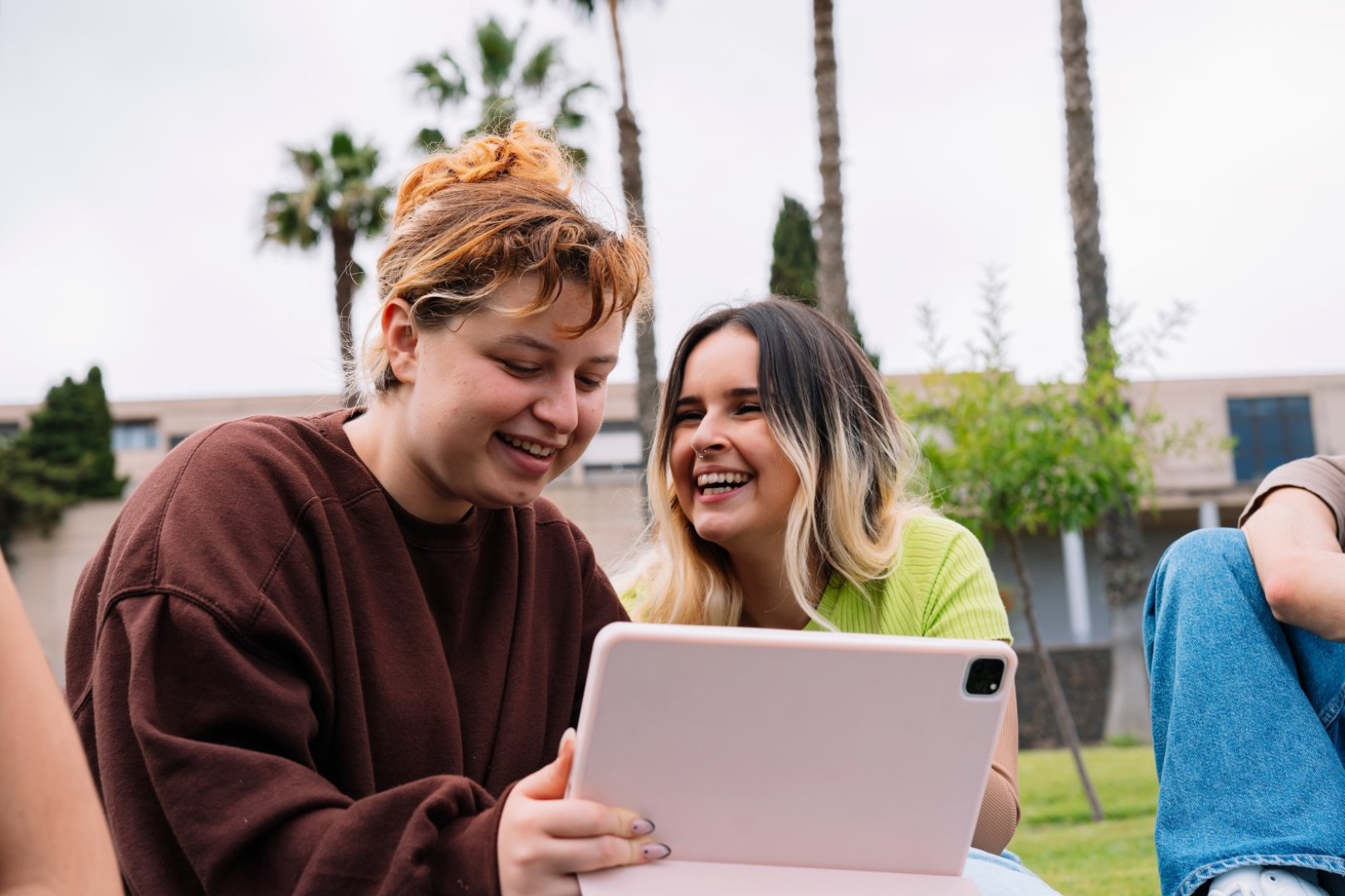 Two women smile while looking at a tablet screen