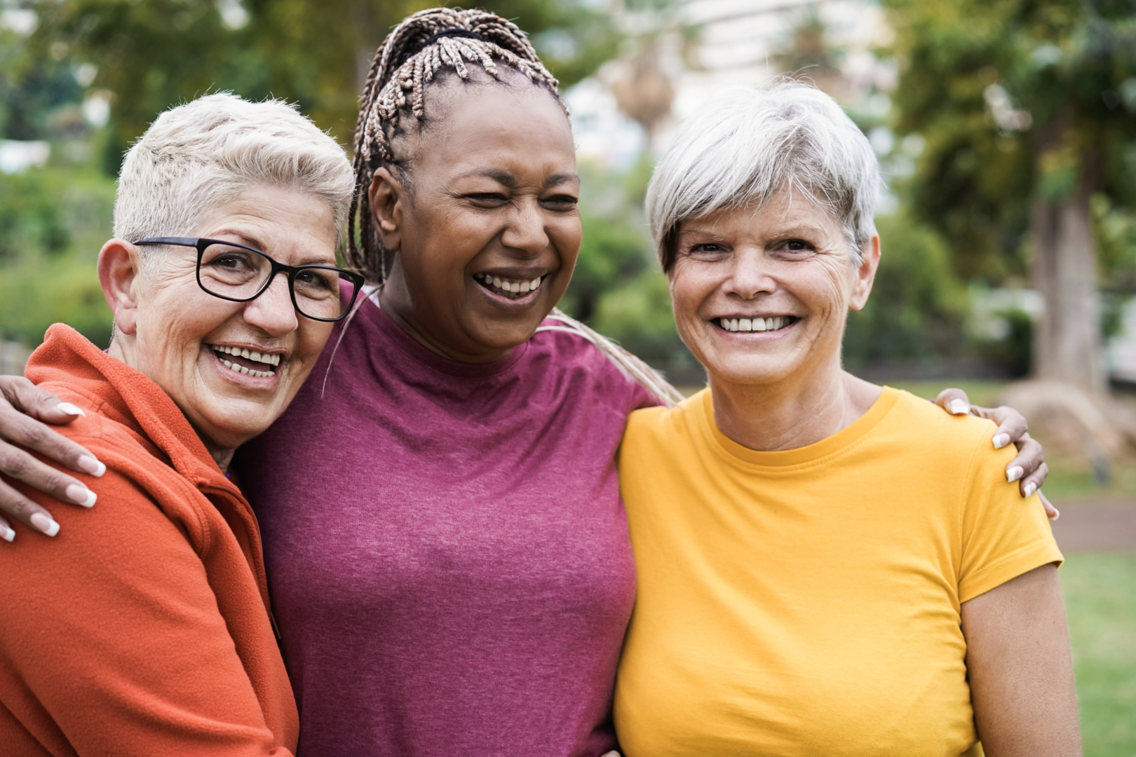 Three older women stand outdoors with their arms around each other