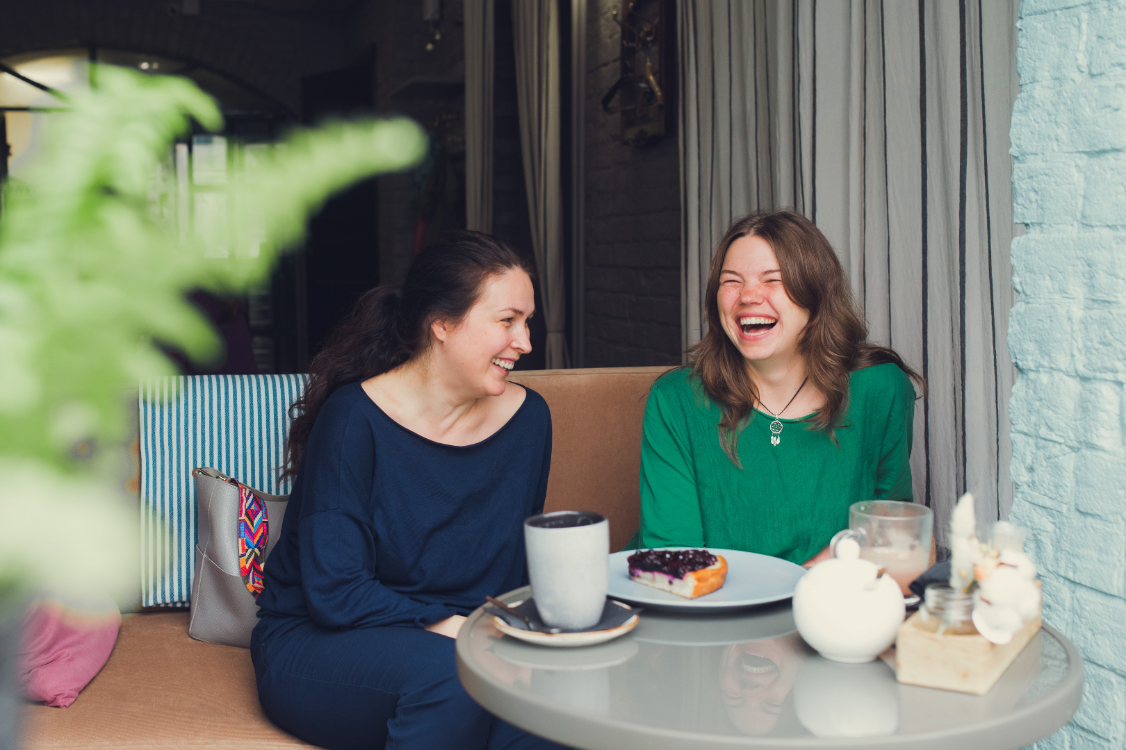 Two women sitting outside with coffee cups laughing together