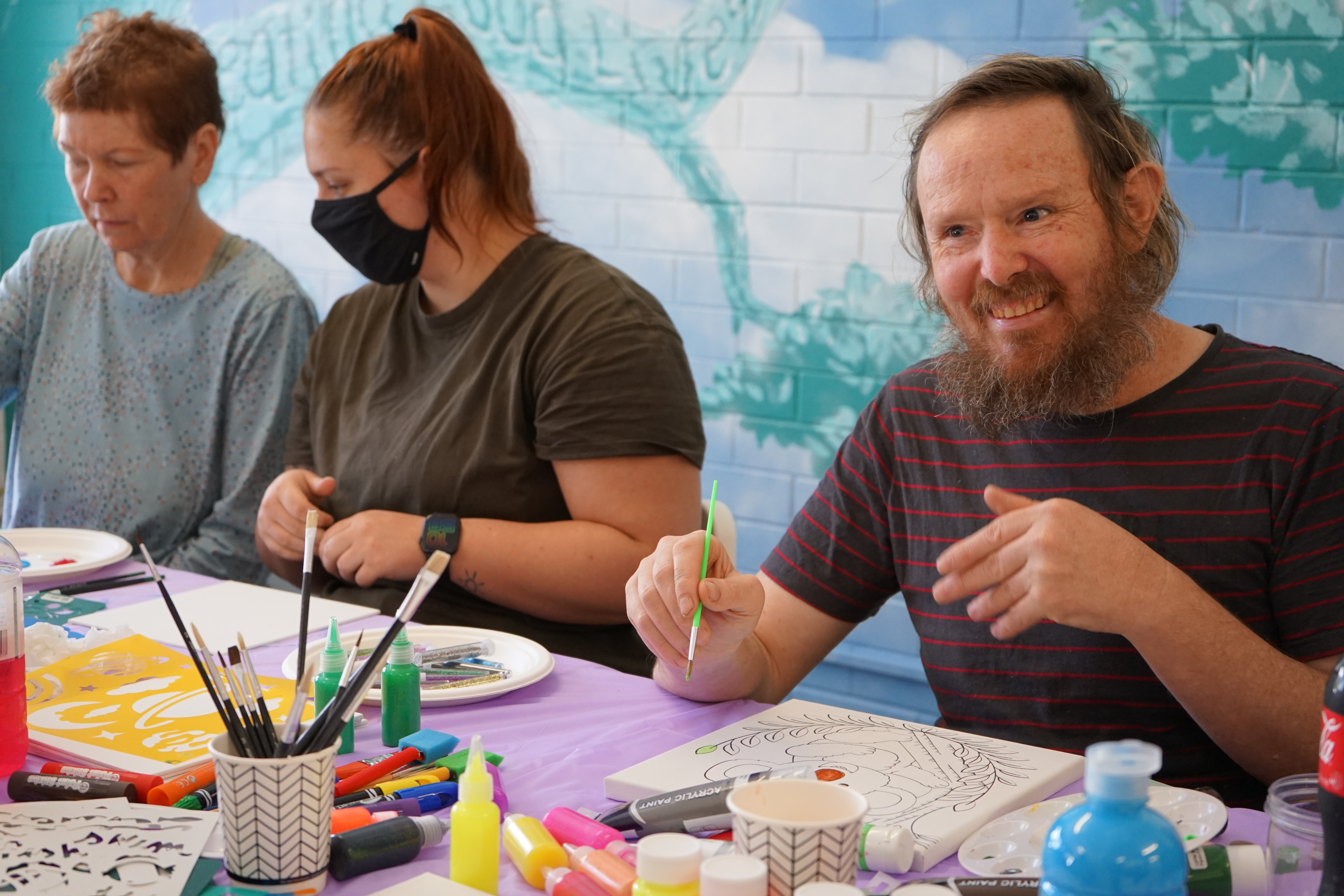 A smiling man paints while two women paint in the background