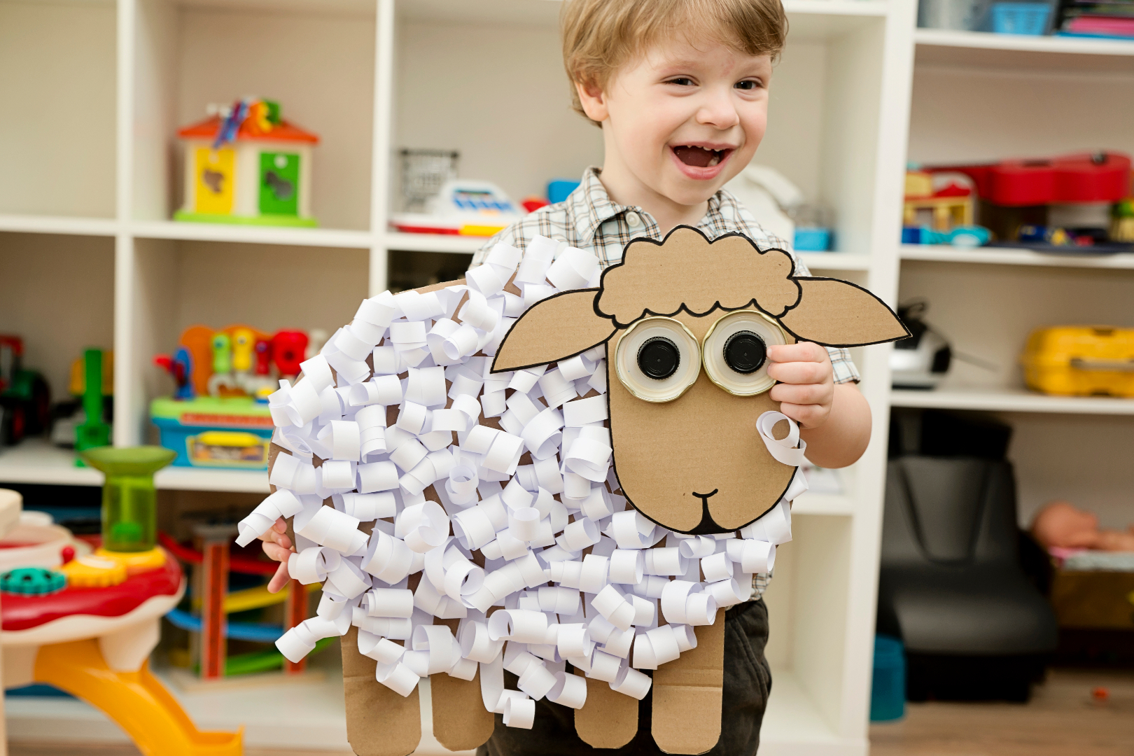 A young boy holds a crafted sheep made of cotton balls and cardboard