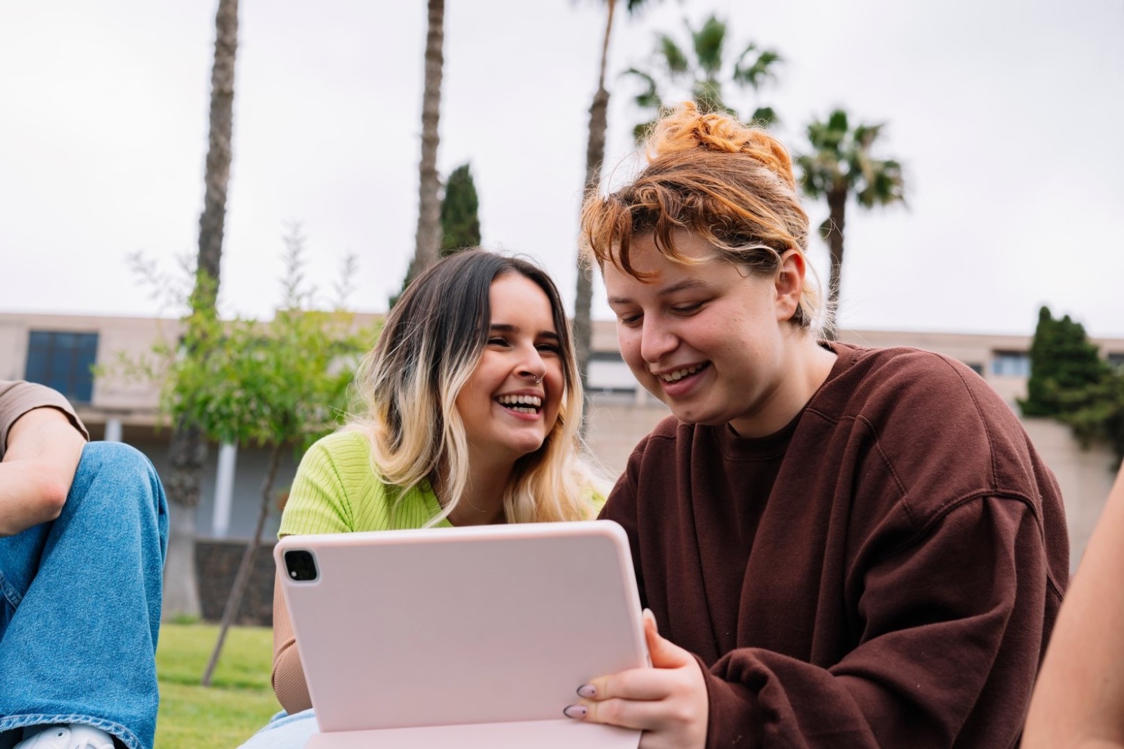 Two women smile while looking at a tablet screen