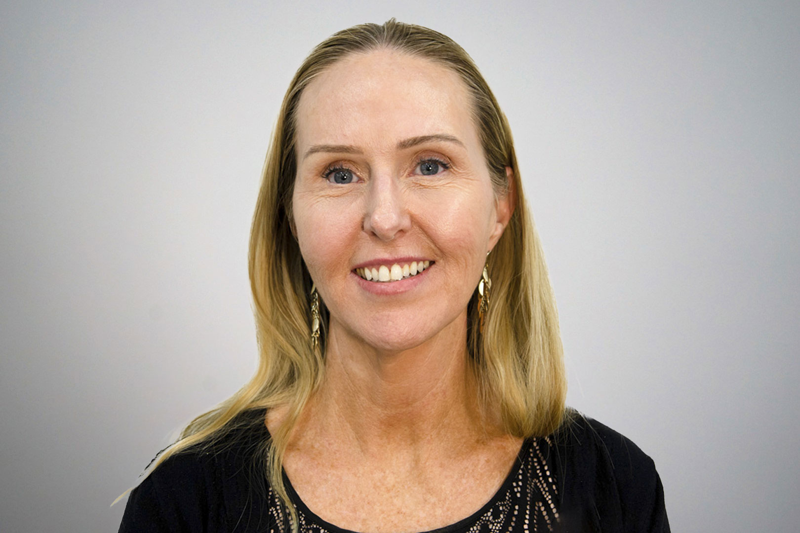 A photo of board member Victoria smiling at the camera on a grey background