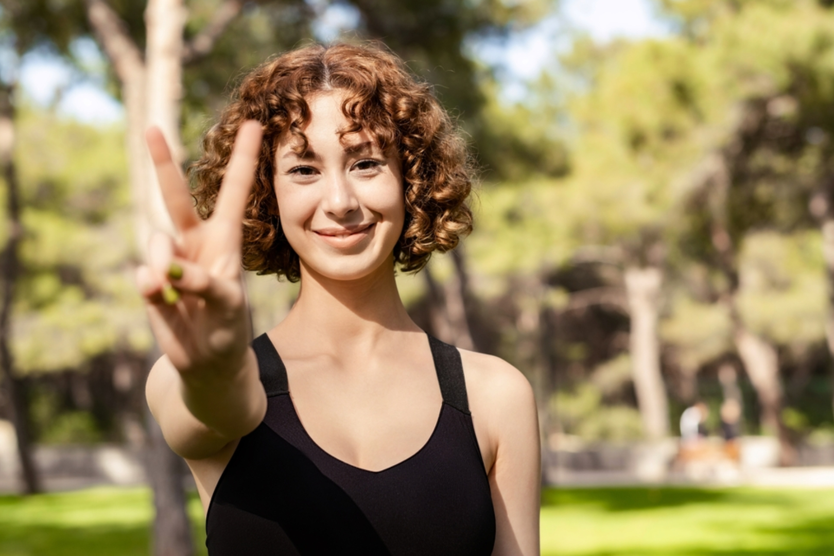 A young woman stands outside and holds her hand up in a peace symbol