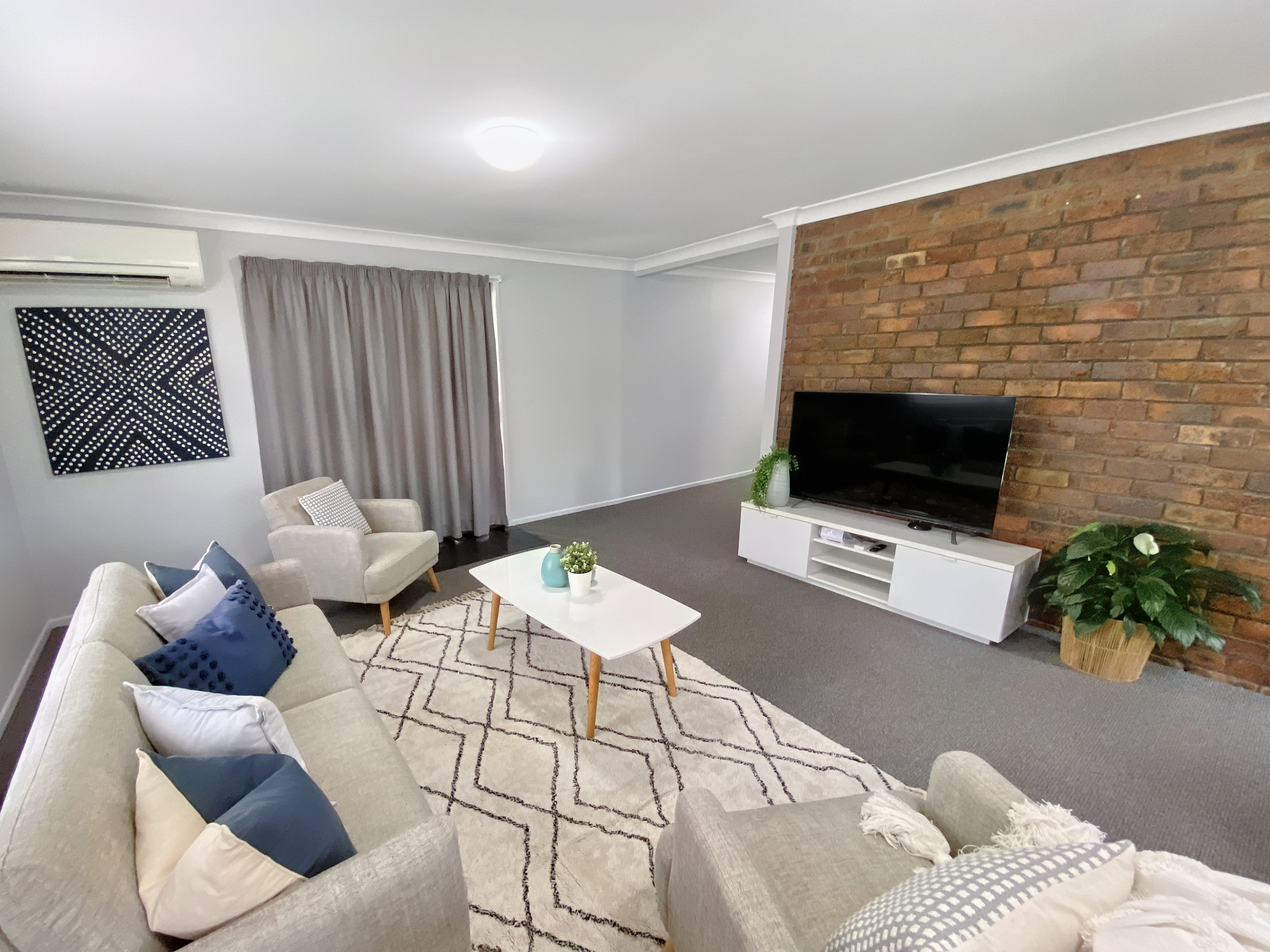 wide angle photo of loungeroom furnished with sofas, rug, coffee table, and large television