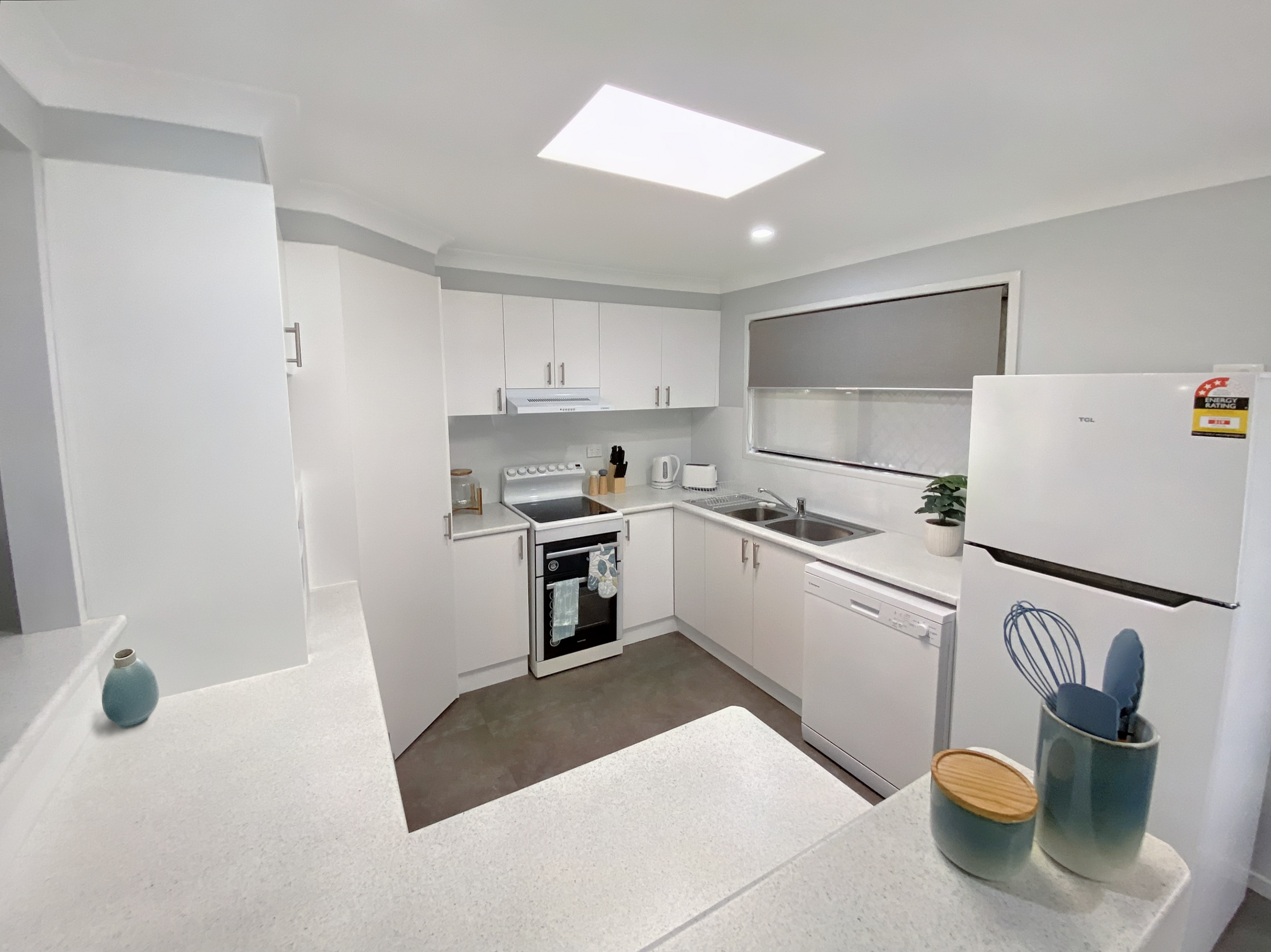 Kitchen with white table tops and cabinets, a skylight, electric oven, dishwasher and fridge. 