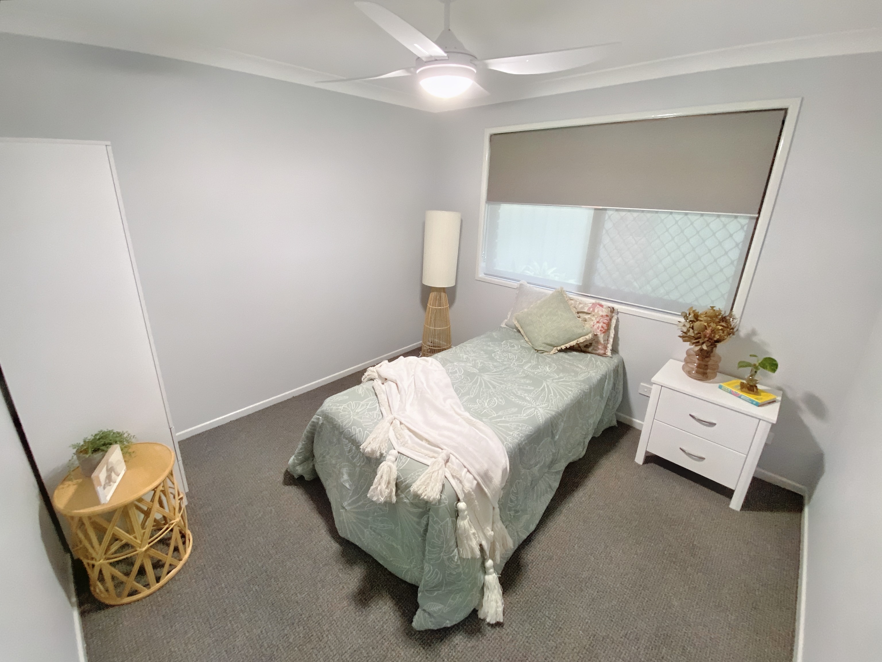 A bedroom with a single bed, bedside table, wardrobe and ceiling fan. The bed has a light green bedspread. 