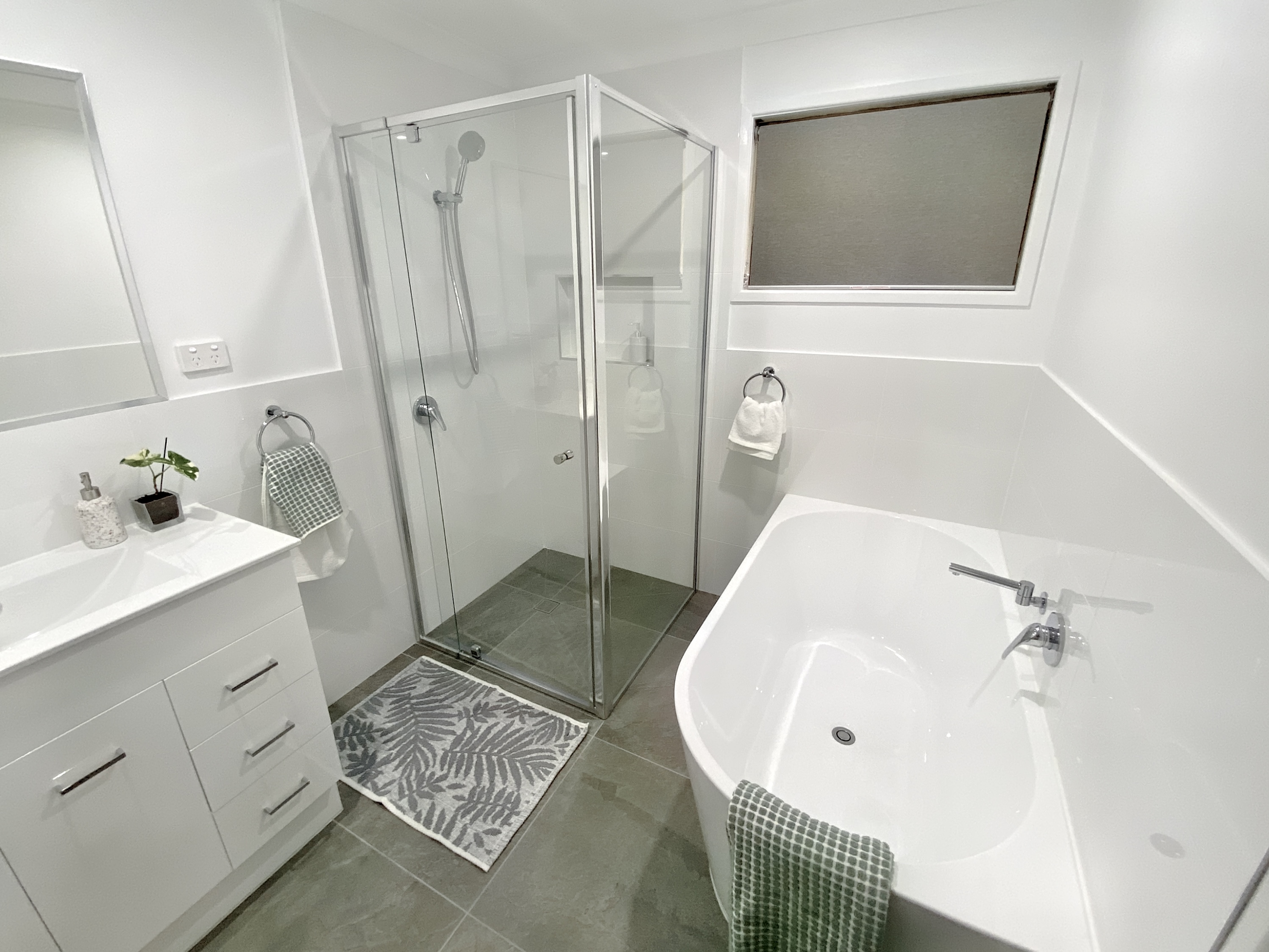 Bathroom with tiled floor and white walls. A large modern bath is on the right wall and a seperate shower with glass shower screens is on the left wall. 