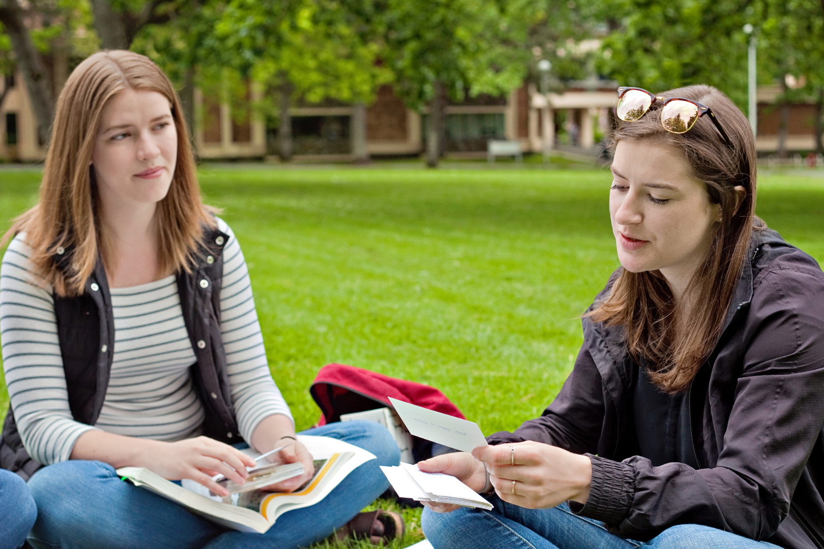 Two women sit outside. One women is reading from a card and the other is looking at her and smiling