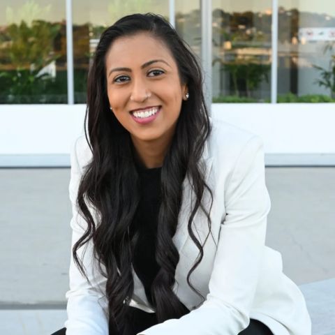 Sheetal Deo smiling and sitting on a concrete bench